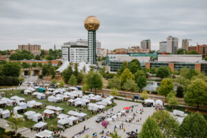Drone view flying above the dogwood arts festival downtown knoxville tennessee with downtown skyline and sunsphere in background with event tents at worlds fair park.
